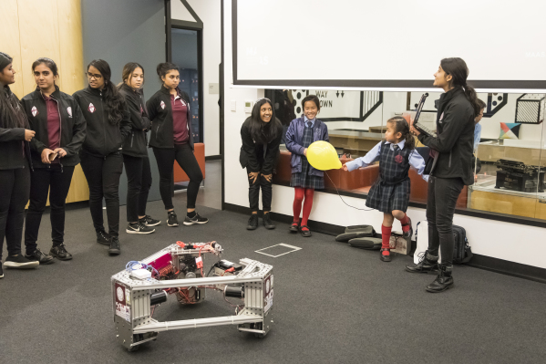 Teenagers showing primary schoolers how to drive a romote-controlled robot.